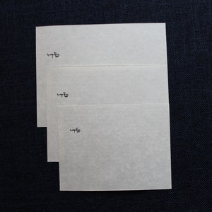 Pu&ograve; includere: Tre pezzi di carta rettangolari bianchi con la parola ebraica "שלו" scritta su ciascuno.