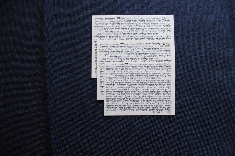 Pu&ograve; includere: Tre carte bianche con testo ebraico stampato in inchiostro blu. Il testo &egrave; in un carattere ebraico tradizionale e include le parole "Shema Yisrael" e "Adonai Eloheinu Adonai Echad".