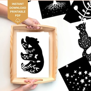Könnte beinhalten: Ein Holztablett enthält eine Sammlung von schwarz-weißen Drucken. Ein Druck zeigt eine Bärensilhouette mit floralen Details. Weitere Drucke zeigen einen Fuchs, Sterne und botanische Designs. In der oberen linken Ecke befindet sich ein goldenes Etikett mit dem Text "INSTANT DOWNLOAD PRINTABLE PDF".