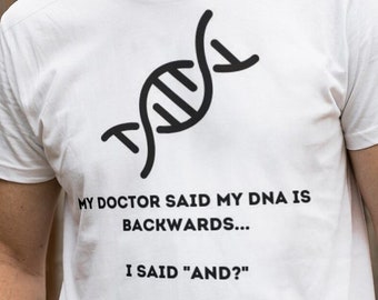 Puede incluir: Camiseta blanca con un gráfico de cadena de ADN negro y el texto "MY DOCTOR SAID MY DNA IS BACKWARDS... I SAID "AND?""