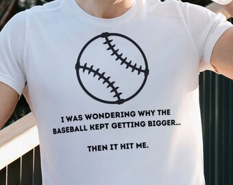 Puede incluir: Camiseta blanca con un gráfico de béisbol negro y el texto "Me preguntaba por qué la pelota de béisbol seguía creciendo... Entonces me golpeó."