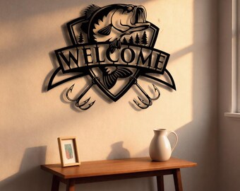 Może przedstawiać: Czarna metalowa grafika ścienna z motywem ryby, napisem "WELCOME" i haczykami wędkarskimi. Zamontowana na jasnej ścianie. Małe zdjęcie w ramce i biały dzbanek stoją na drewnianym stole. Stół ma 100 cm długości.