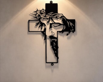 Może przedstawiać: Czarna metalowa grafika ścienna przedstawiająca Jezusa Chrystusa na krzyżu. Grafika przedstawia szczegółowy kontur twarzy Jezusa, koronę cierniową i brodę. Krzyż ma prosty, obrysowany kształt, odpowiedni do dekoracji religijnych.