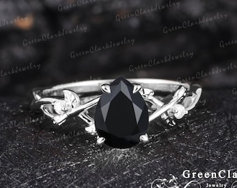 May include: A pear-shaped black onyx engagement ring set in a silver band with a delicate vine design.