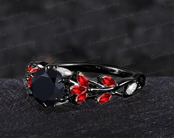 May include: Black engagement ring with a large black gemstone surrounded by smaller red gemstones. The ring band is black and features a delicate floral design.