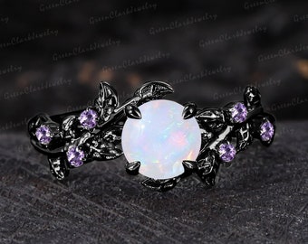 May include: A black metal ring featuring a large, round, white opal gemstone as the centerpiece. The ring is adorned with delicate leaf and vine detailing, accented by small, purple gemstones. The ring is set against a dark, textured background.