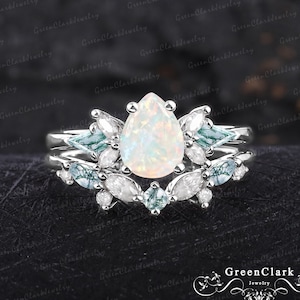May include: A pear-shaped opal engagement ring set with a silver band and delicate floral accents. The ring features a large opal stone surrounded by smaller diamonds and aquamarine stones.