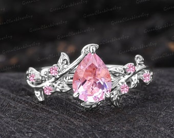 May include: A pear-shaped pink gemstone ring with a delicate floral design. The ring is set in silver and features small pink gemstones on the band.