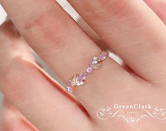 May include: A delicate rose gold ring with a floral design featuring small pink gemstones. The ring is on a finger and the background is blurred.