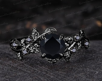 May include: Black engagement ring with a large black gemstone surrounded by smaller black gemstones. The ring band is black and features a leafy design.