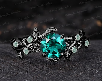 May include: A black ring with a large, round, emerald-green gemstone at the center. The ring features a floral design with leaves and smaller, light-green gemstones. The ring is set against a dark, textured background.