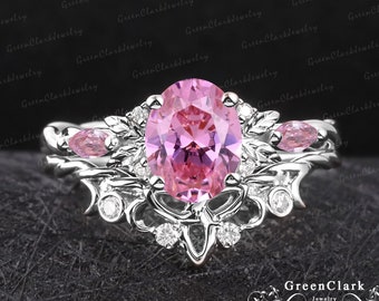 May include: A silver ring with a large oval pink gemstone surrounded by smaller clear gemstones. The ring has a delicate, floral design.