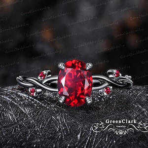 Può includere: Un anello in metallo nero con una grande pietra rossa a taglio ovale tenuta da quattro griffe. La fascia presenta un design intrecciato a forma di vite, impreziosito da quattro pietre rosse rotonde più piccole, due su ogni lato del castone.