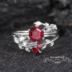 May include: A silver ring featuring a red gemstone and white diamonds set in a leafy design. The ring is displayed against a black background with the text "GreenClark Jewelry" in white.