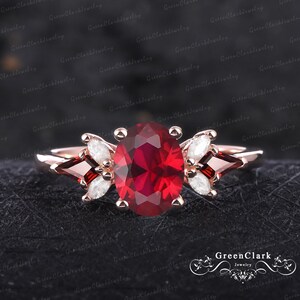 May include: A rose gold engagement ring featuring a large oval ruby gemstone, surrounded by smaller white and red gemstones.