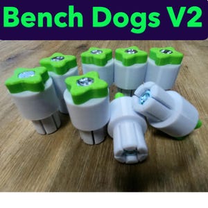 Könnte beinhalten: Eine Sammlung weißer und grüner Bench Dogs V2. Jeder Bankhund hat einen weißen zylindrischen Körper mit einer grünen, sternförmigen Oberseite. Der Text "Bench Dogs V2" wird in grünen Buchstaben auf dunklem lila Hintergrund angezeigt.