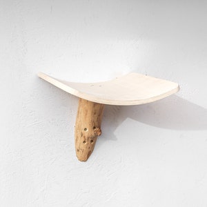 Könnte beinhalten: Ein Holzregal mit einer gebogenen Oberseite und einem Sockel aus natürlichem Ast. Das Regal ist aus hellem Holz gefertigt und hat eine natürliche Oberfläche. Der Astsockel ist mit Schrauben am Regal befestigt.