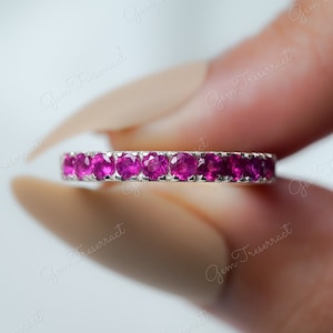 May include: A delicate eternity band ring with a row of small, round, pink gemstones set in a silver band.