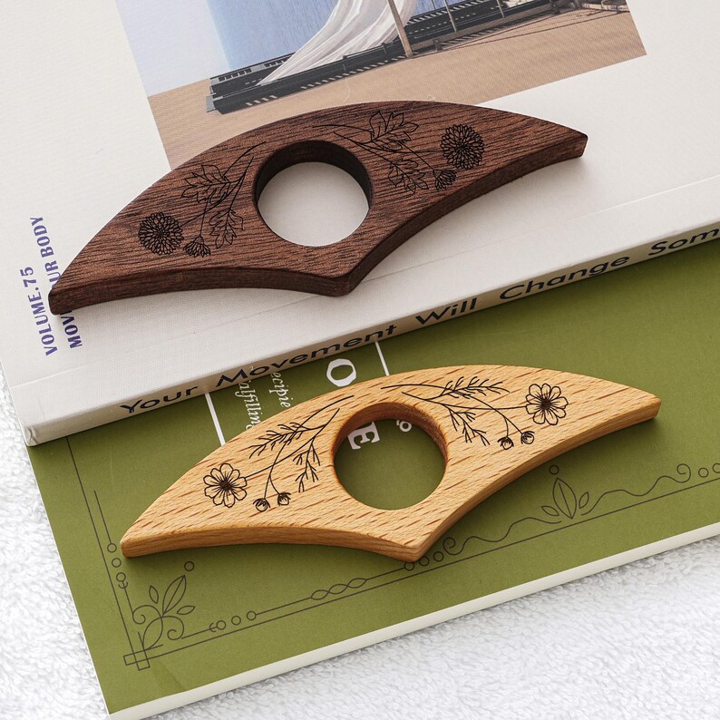 Puede incluir: Dos sujetalibros de madera con dise&ntilde;os florales. Uno es marr&oacute;n oscuro, el otro es marr&oacute;n claro. Cada uno tiene una abertura circular para el dedo. Los sujetalibros est&aacute;n sobre un libro con el texto "Your Movement Will Change Some".