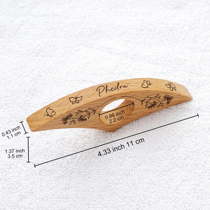 Puede incluir: Un sujetap&aacute;ginas de madera con el nombre "Phedra" grabado. El soporte mide 11 cm de largo y presenta dise&ntilde;os de mariposas y flores. Tiene un orificio para el dedo y mide 2,2 cm de ancho.