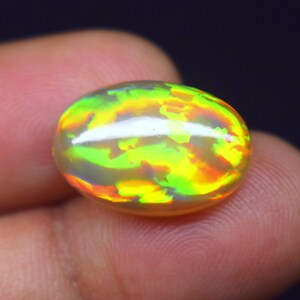 May include: An oval-shaped cabochon opal gemstone displaying a vibrant play-of-color with bright flashes of neon green, yellow, and orange against a translucent, milky white base. The stone features a smooth, polished, and domed surface.