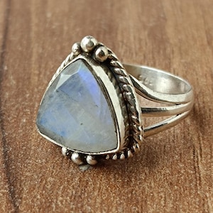 May include: A silver ring with a triangular moonstone set in a silver bezel. The ring has a braided band with small silver beads.