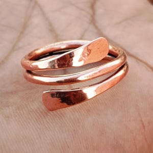 May include: A copper-coloured spiral ring with an open design. The ring wraps around the finger with two flared ends. The ring is made of a shiny, metallic material.