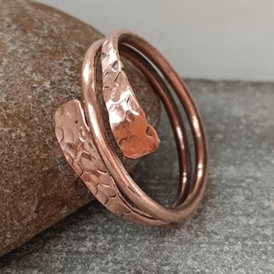 May include: A hammered copper ring with a spiral design. The ring is made of two bands of copper that are twisted together.