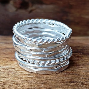 May include: A stack of silver rings with different textures and designs. The rings are stacked on top of each other, creating a unique and stylish look.