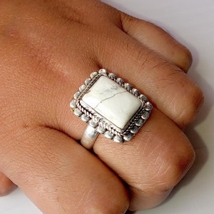 May include: A silver ring with a white rectangular stone set in a decorative border.
