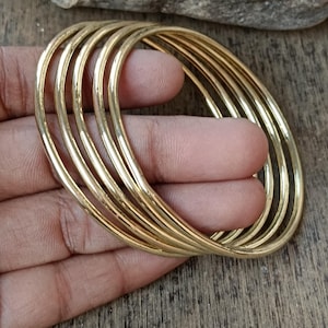 May include: A set of six gold-toned bangle bracelets. The bracelets are stacked on top of each other and are made of a smooth, shiny metal.