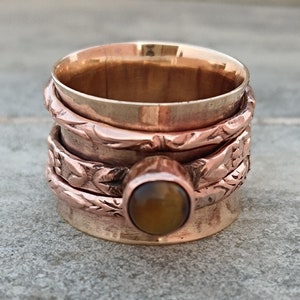May include: A copper spinning ring with a brown tiger's eye gemstone. The ring has a decorative design of leaves and vines.