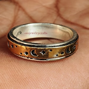 May include: A silver and gold spinning ring featuring a design of moons and stars. The ring is engraved with the text "omjewelrycrafts".