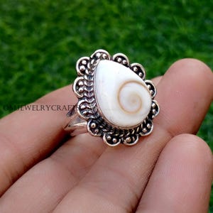 May include: A silver ring with a large, teardrop-shaped white stone with a spiral pattern. The stone is set in an ornate silver setting with a scalloped edge. The ring is a piece of jewellery.