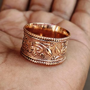 May include: A wide, gold-toned ring with a floral design. The ring is made of metal and has a textured surface.