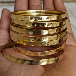 Op de afbeelding: Een stapel van zes gouden, gehamerde metalen armbanden. De armbanden zijn op elkaar gestapeld en zijn allemaal even groot.