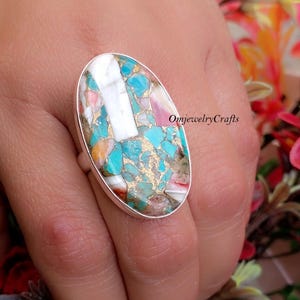 Op de afbeelding: Ovale ring met een turquoise, witte en roze steen gezet in zilver. De steen is gemaakt van veel kleine stukjes turquoise, wit en roze.