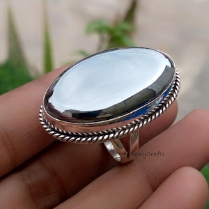 Op de afbeelding: Een zilveren ring met een grote, ovale, gepolijste, lichtgekleurde steen. De steen is gezet in een zilveren band met een gedraaid touwontwerp rond de rand. De ring zit aan de hand van een persoon. De tekst "onlyjewelrycrafts" is zichtbaar.