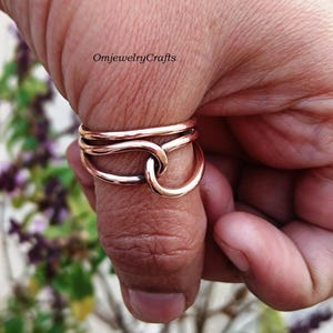May include: A copper thumb ring with a twisted design. The ring is made of three bands of copper wire that are twisted together to form a knot. The ring is worn on a person's thumb.