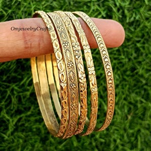 Op de afbeelding: Set van vijf gouden metalen armbanden met ingewikkelde bloemmotieven. De armbanden zijn op elkaar gestapeld.