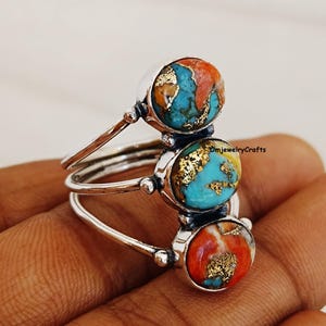 May include: Silver ring featuring three stacked stones. The stones are a combination of turquoise, coral, and gold.