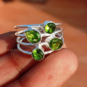 Può includere: Un anello d'argento con quattro pietre preziose di peridoto verde. L'anello è impilato con tre bande.
