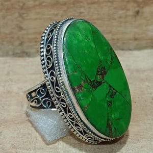 May include: A silver ring with an oval-shaped green gemstone set in a filigree design.