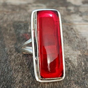 May include: A silver ring with a large, rectangular, red gemstone.