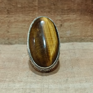 May include: A silver ring featuring a large oval tiger's eye gemstone. The stone is brown and gold in colour with a chatoyant effect.