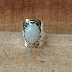 Könnte beinhalten: Ein silberner Ring mit einem großen ovalen weißen Edelstein, der in eine silberne Fassung gefasst ist.