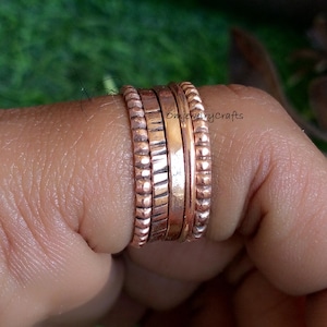 May include: A set of four copper rings stacked on a finger. The rings are all different widths and have a hammered texture. The rings are a warm copper color.