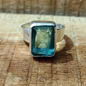 Può includere: Un anello d'argento con una grande pietra preziosa blu rettangolare a taglio smeraldo.
