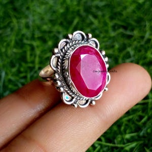 May include: A silver ring with a large, oval-shaped, faceted ruby gemstone set in a detailed, ornate silver setting. The ring is on a finger.