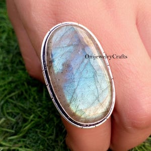Könnte beinhalten: Ein silberner Ring mit einem großen ovalen Labradorit-Edelstein. Der Edelstein hat einen blauen, grünen und goldenen irisierenden Schimmer.
